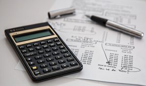 An image of a calculator, a pen and a sheet of paper showing some tabled figures.