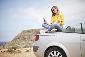 Young smiling woman sitting on top of an expensive sports car